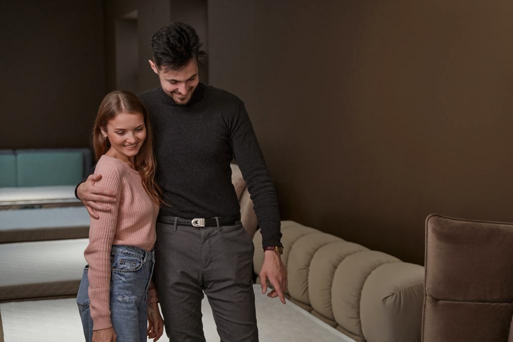 Couple standing among beds with mattresses in shop.