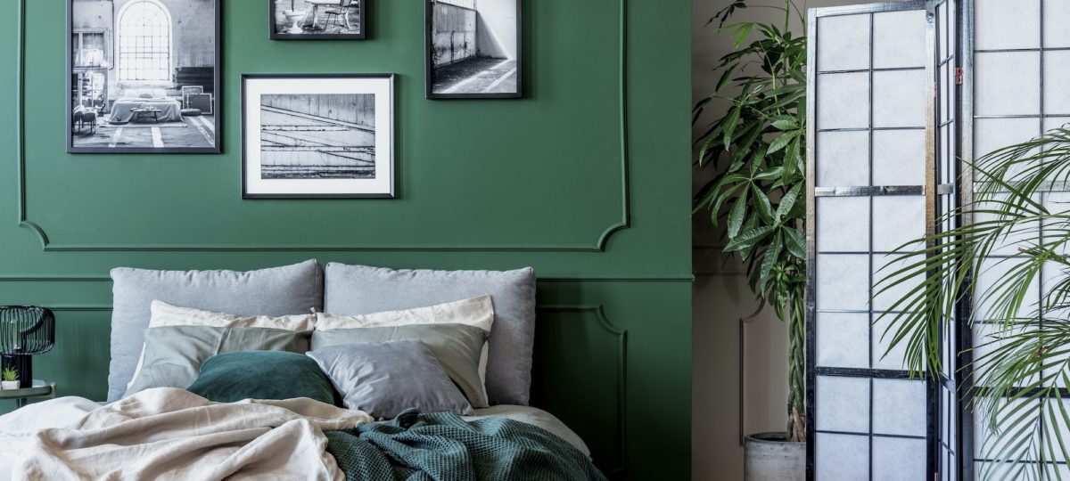 Gallery of black and white posters and photos on emerald green wall in trendy bedroom