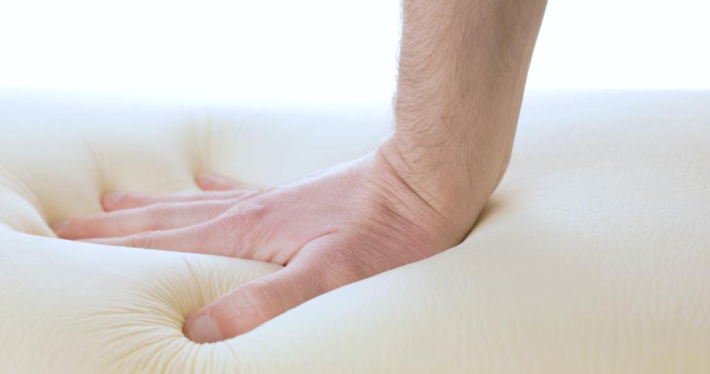 A hand is pressing a memory foam mattress. What to do before buying a latex mattress.