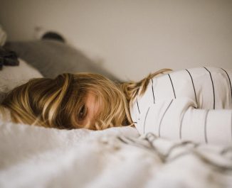 How Many Hours Of Sleep Should You Be Getting Each Night? Woman looking tired on a bed.