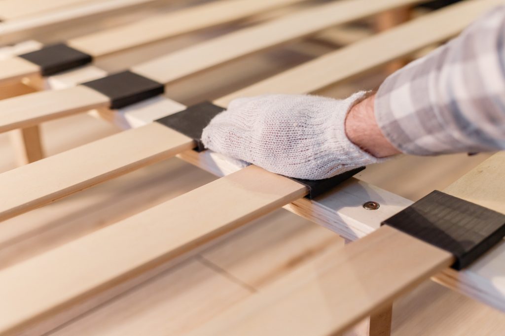 Male worker's hand in glove assembling bed, connecting slats to a heavy duty bed frame. Frames or boxsprings?