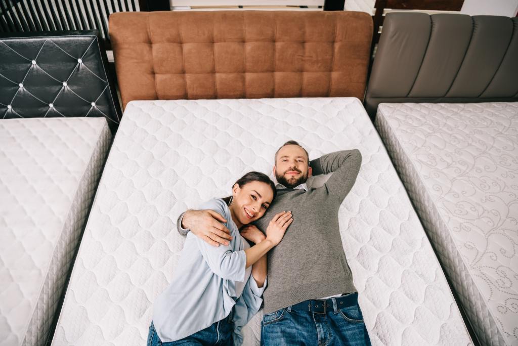 overhead view of smiling couple testing a bed before buying it in the mattress store.