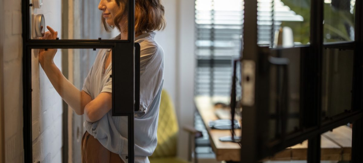 Woman controlling temperature with a thermostat at home