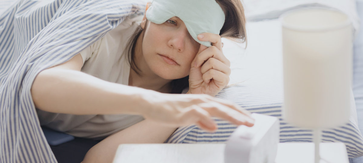 Woman in bed with a sleep mask wakes up and turns off the alarm. a clock with a timer, a woman yawns.