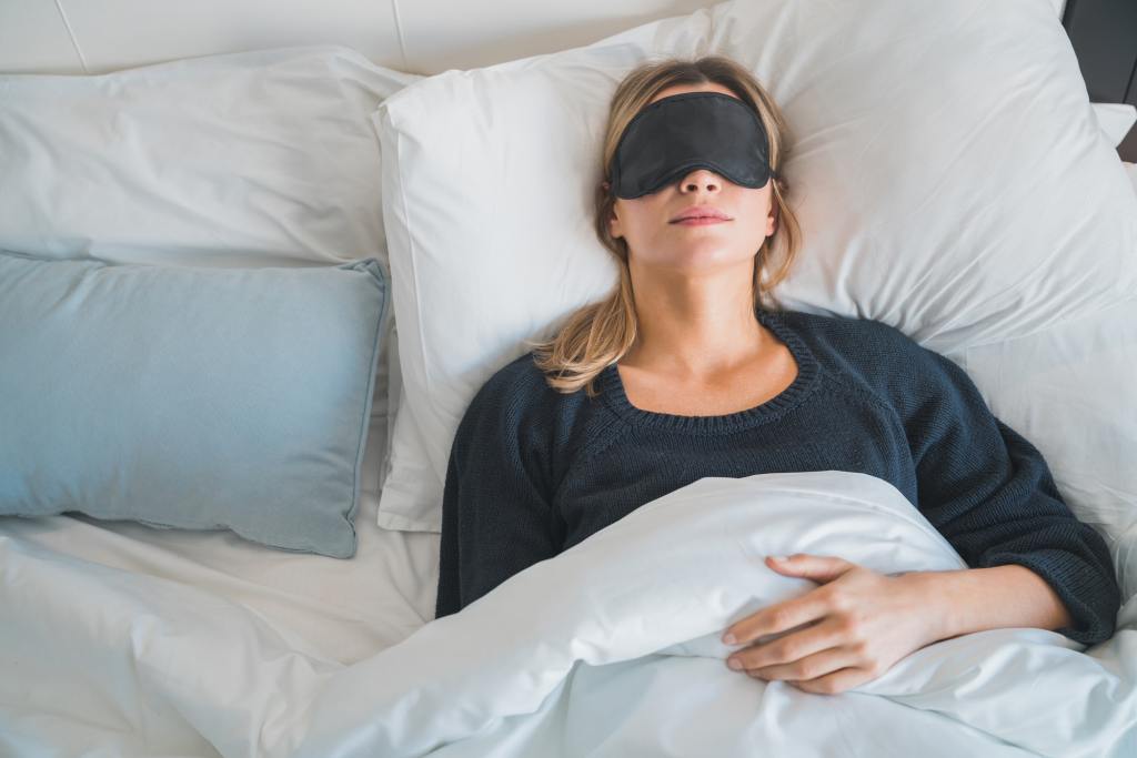 Woman using an eye mask to help her sleep through one of the sleep cycles.