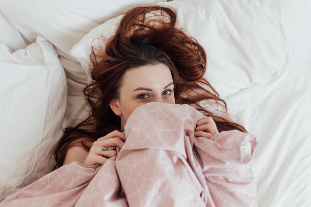 A young redhead woman under bedsheets is comfortable because of the thread count she picked.